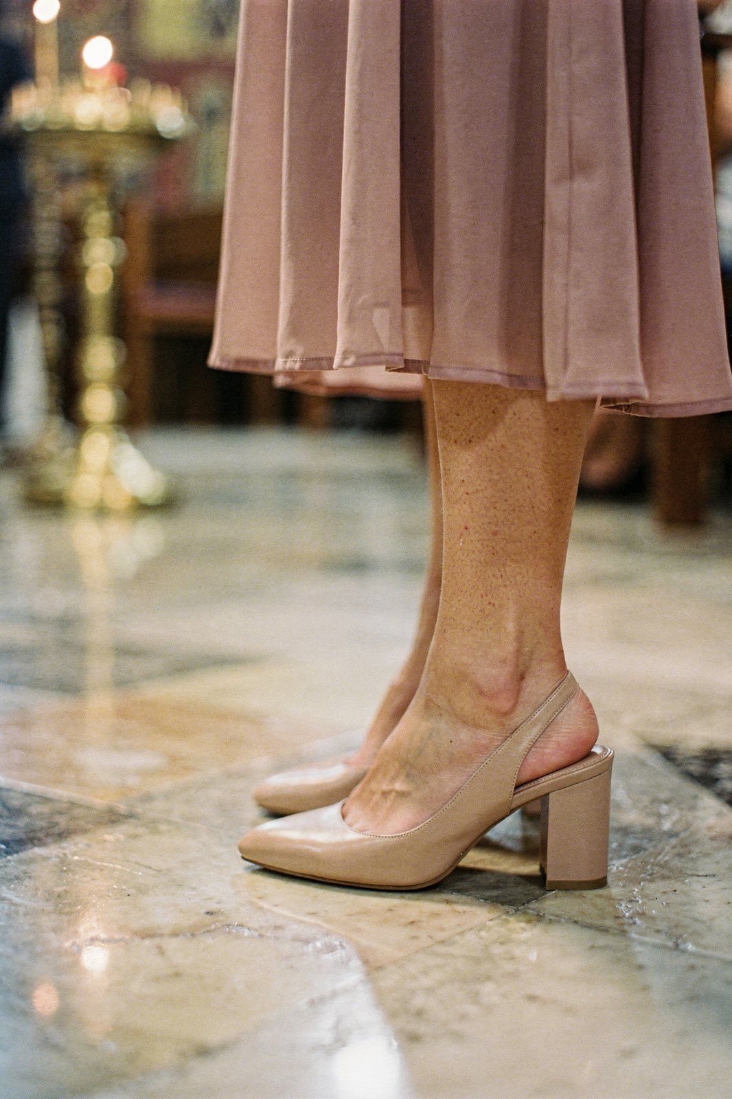 Nude γόβες slingback με κλειστή μύτη και φαρδύ τακούνι κάτω από ροζ μίντι φόρεμα, σε μαρμάρινο δάπεδο εκκλησίας